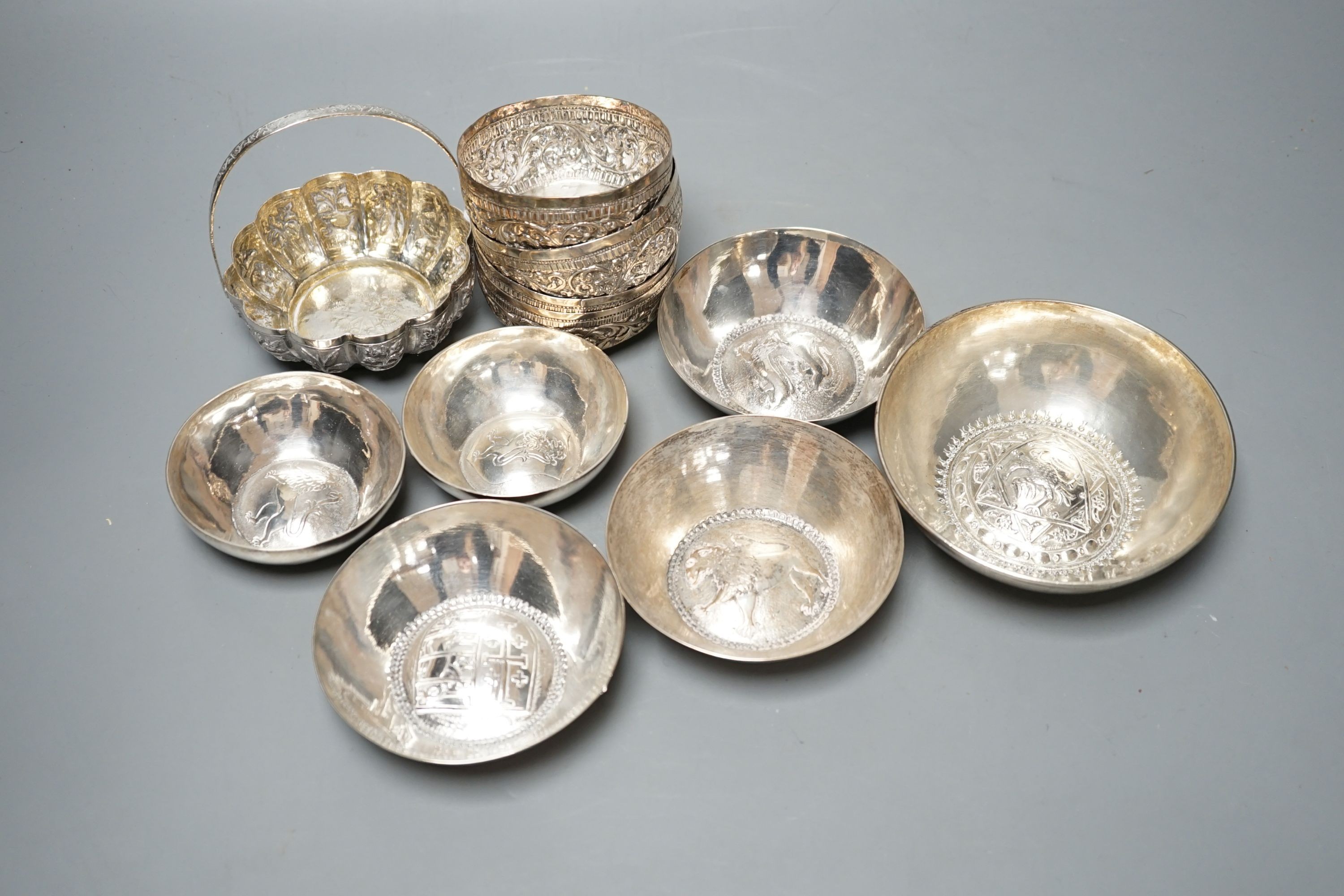 Four small Rangoon white metal bowls together with a simile basket and six small white metal bowls with heraldic motifs, gross 24.5oz.